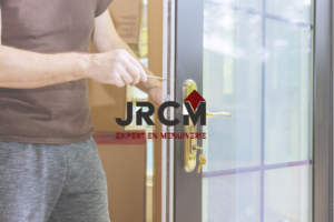 Logo de la société JRCM avec, en fond, une personne en train de travailler sur une porte à l'aide d'un tournevis