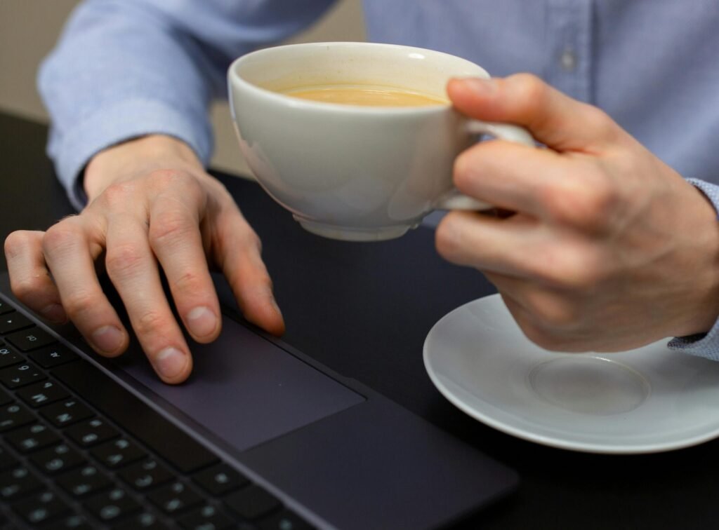 Homme pianotant sur un ordinateur portable en buvant un café