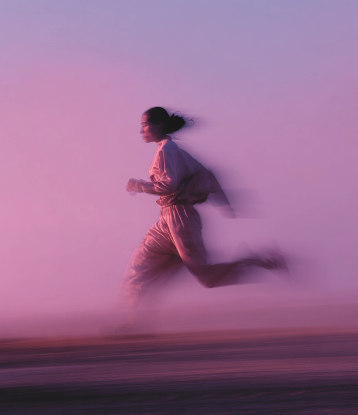Femme courant dans un paysage flou avec des tons pastel, capturée en mouvement avec un effet de vitesse.