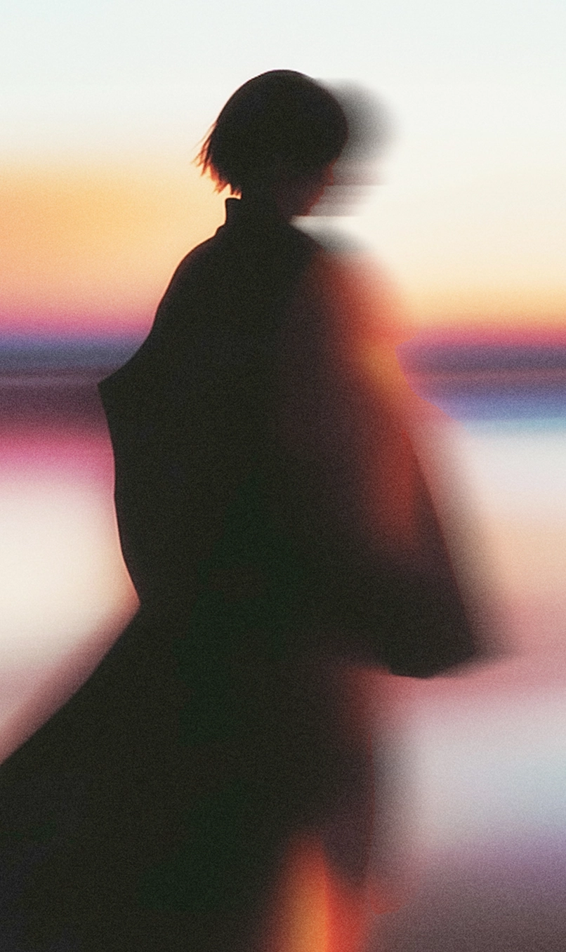 Silhouette floue d’une personne portant un vêtement ample devant un fond aux couleurs du crépuscule.