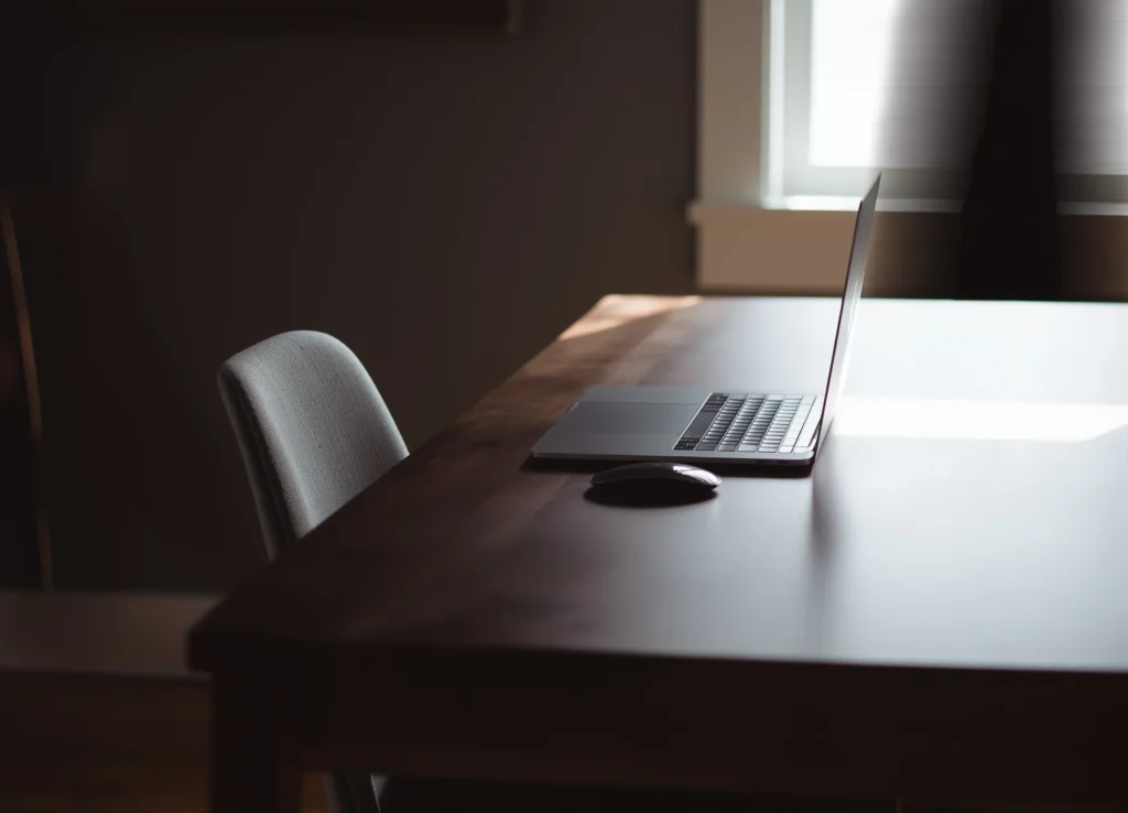 Bureau minimaliste avec un ordinateur portable ouvert, une chaise et une souris, éclairé par une lumière naturelle.